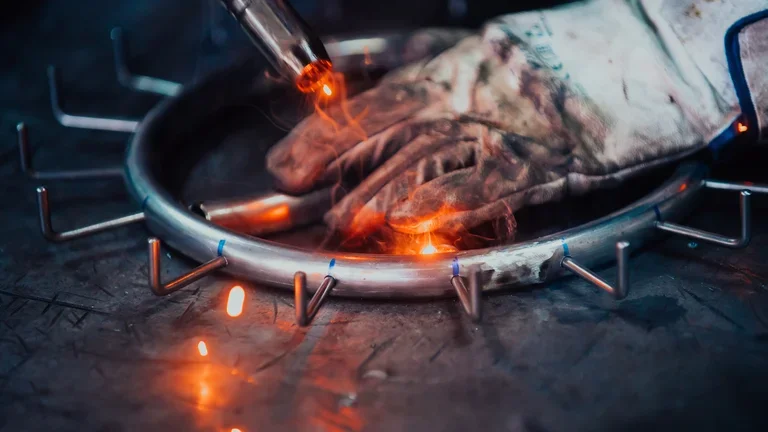 Soldadura en pieza metálica con chispas y guante de protección.